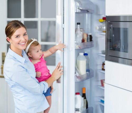Happy,Woman,Opening,Refrigerator,While,Carrying,Baby,Girl,At,Home